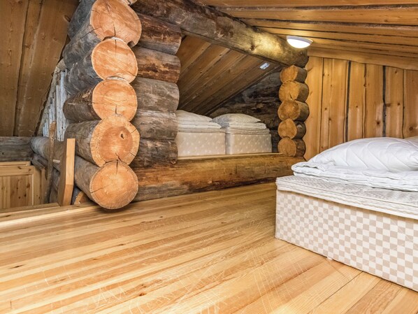 Una habitación tipo cabaña de madera con una cama en el altillo, un colchón en el suelo y piso de madera.