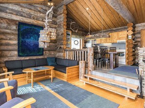 Interior rústico de una cabaña con un sofá, mesas de madera y una zona de cocina.