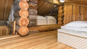 A log cabin bedroom with a wooden floor, a bed with a checkered mattress, and a mattress on the wall.