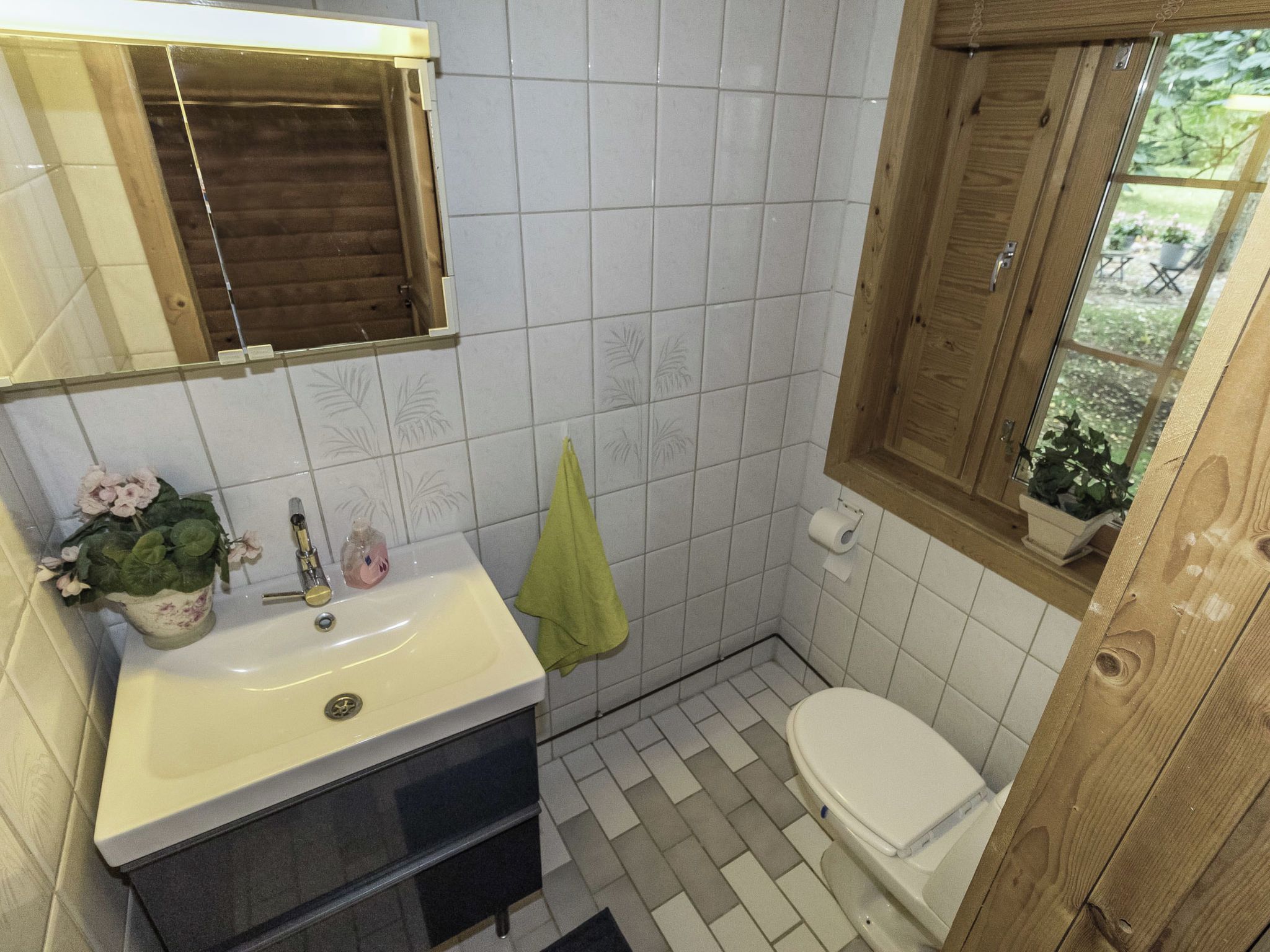 Ein Badezimmer mit einem weißen Waschbecken, einer Toilette und einem Fenster mit Holzklappläden.