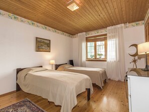 Een kamer met twee bedden, houten vloeren, een raam met gordijnen, een bureau met lamp en een schilderij aan de muur.