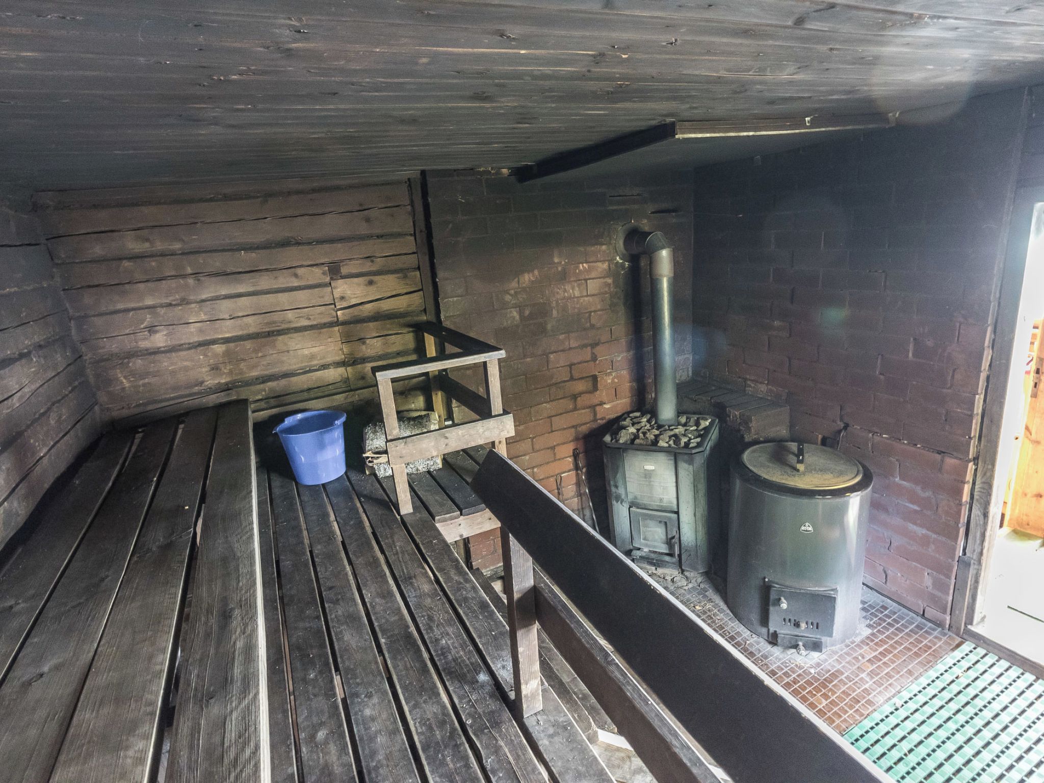 A rustic wooden room with a bench, a blue bucket, and a wood-burning stove.
