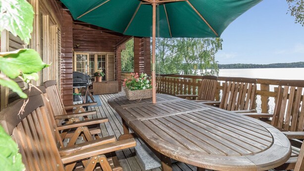 Een houten terras met een tafel, stoelen, een groene parasol en uitzicht op een meer.