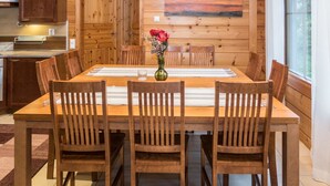 A wooden dining room with a large table, chairs, and a vase of flowers.