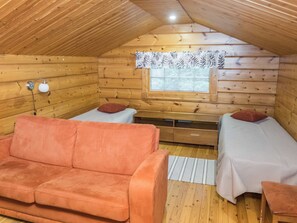 A cozy cabin room with a wooden interior, two single beds, a sofa, a desk, and a window with curtains.