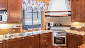 A compact kitchen with wooden cabinets, a stainless steel sink, a built-in oven, and a window with blinds.