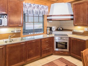A compact kitchen with wooden cabinets, a stainless steel sink, a built-in oven, and a window with blinds.