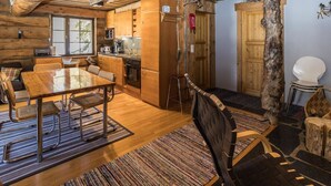 A rustic cabin interior with a wooden dining table, chairs, a kitchen area, and a large window. - Örtsylä a by Interhome (Salla)