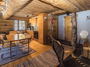 Innenansicht einer Holzhütte mit Essbereich, Küche und einer großen Holztür.