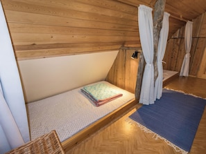 Ein kleiner, holzgetäfelter Dachzimmerraum mit einem Bett, einem Sessel und einem Fenster mit Vorhängen.