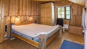 A wooden cabin bedroom with a bed, a window, and a small seating area. - Örtsylä a by Interhome (Salla)