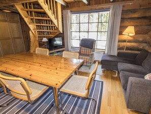 Ein gemütliches Blockhaus-Interieur mit einem Holztisch, einer Couch, einem Sessel und einem Fernseher.
