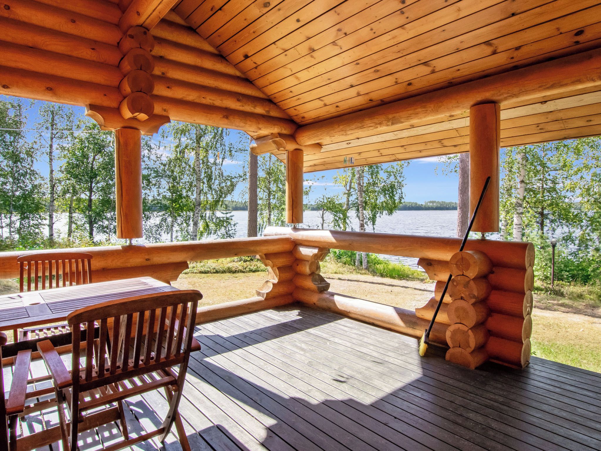 Une terrasse en bois avec une table et des chaises, donnant sur un lac bordé d’arbres.