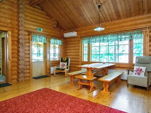Ein Holzblockhaus-Innenraum mit einer hölzernen Bank, einem Tisch, einem Stuhl und einem roten Teppich.