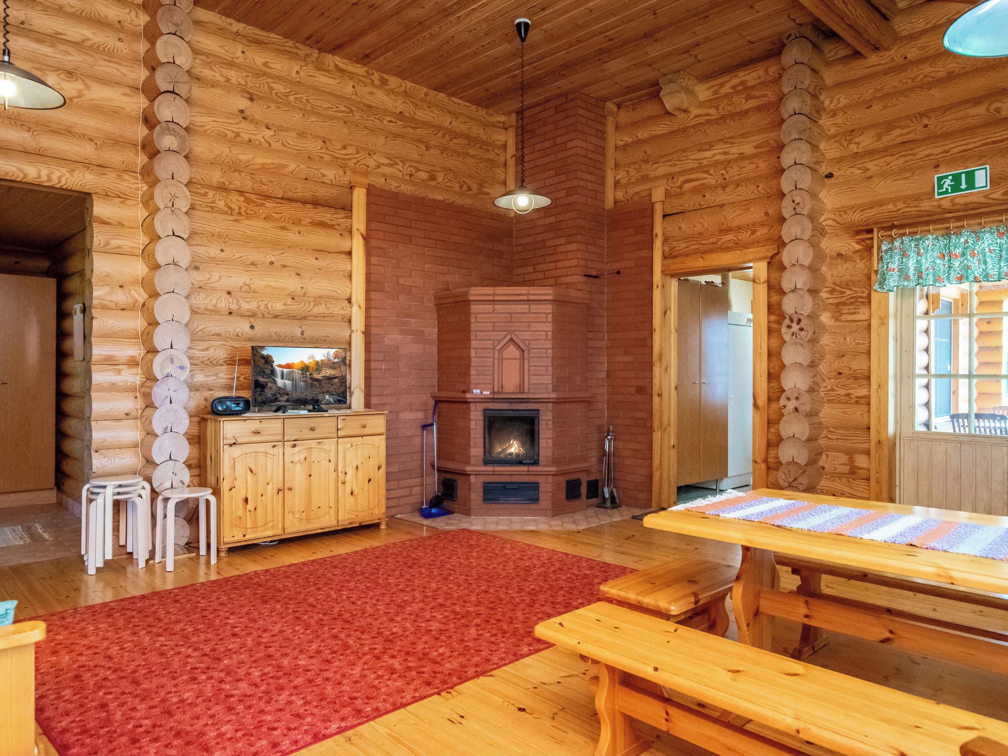 A log cabin interior with a fireplace, wooden furniture, and a red carpet.