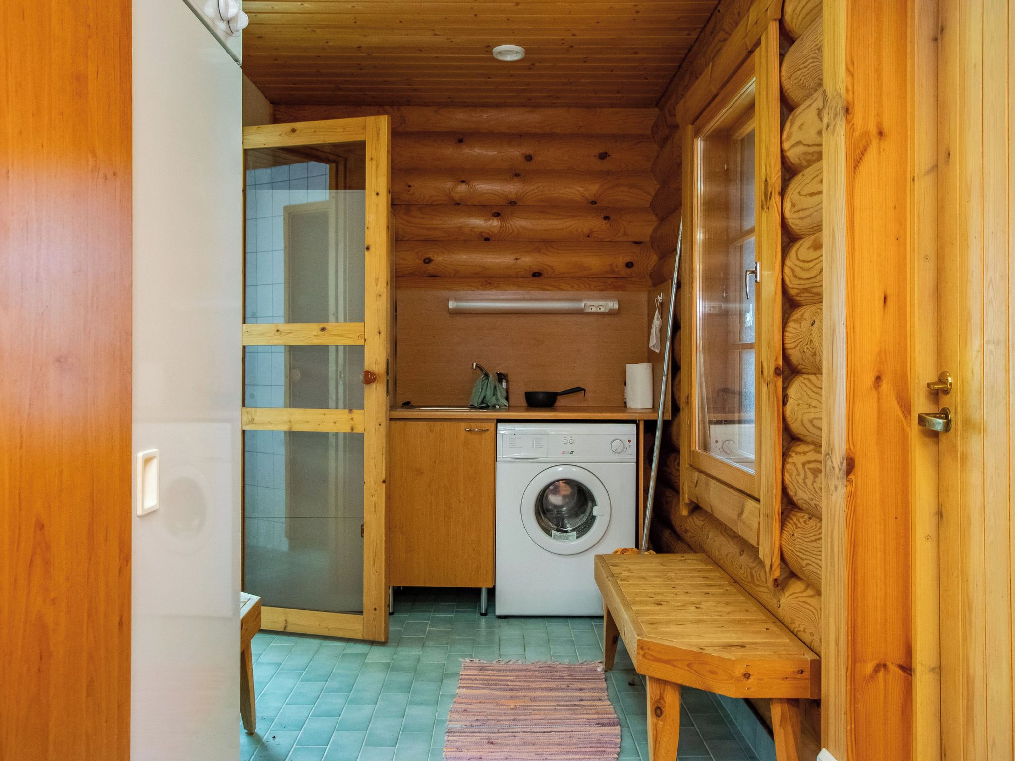 A compact, wooden cabin interior with a washing machine, a small table, and a bench.