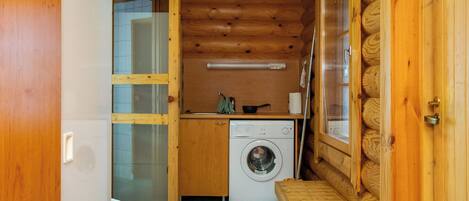 A compact, wooden cabin interior with a washing machine, a small table, and a bench.