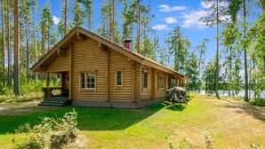 A log cabin with a porch, a chimney, and a view of a lake.