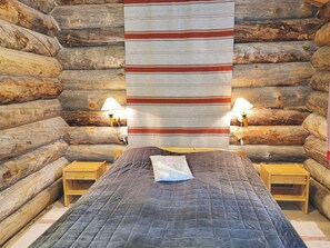 A log cabin room with a bed, two bedside lamps, and a large striped blanket.
