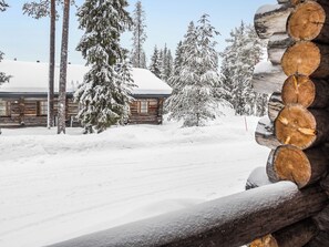 A log cabin with a snow-covered roof, surrounded by snow-laden trees, and a clear sky.
