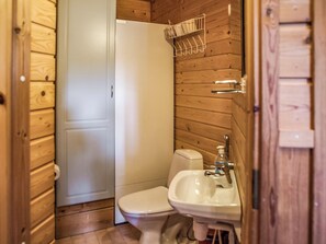 Une petite salle de bain aux murs lambrissés, équipée de toilettes, d’un lavabo et d’une porte blanche.