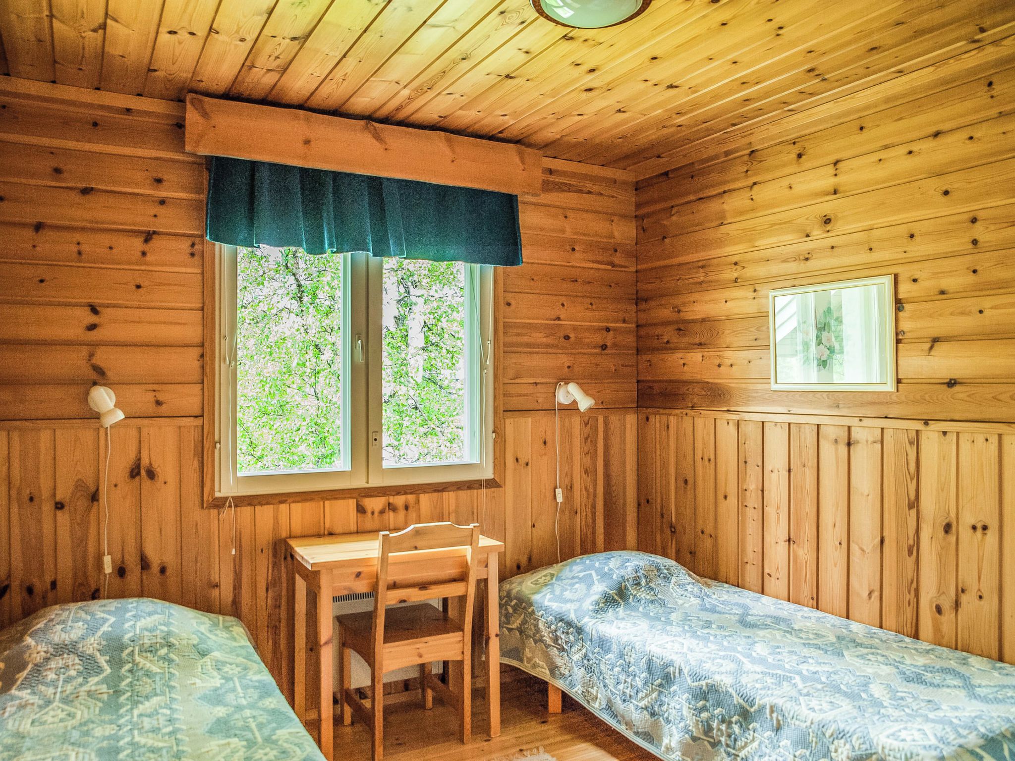 Eine Hütte mit zwei Holzbetten, einem Schreibtisch und einem Fenster mit Blick auf Grünfläche.