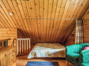 A room with a sloped ceiling, a bed with a quilted cover, a wooden dresser, a chair, and a patterned rug. - Vacation home Kallio by Interhome (Kuusamo)
