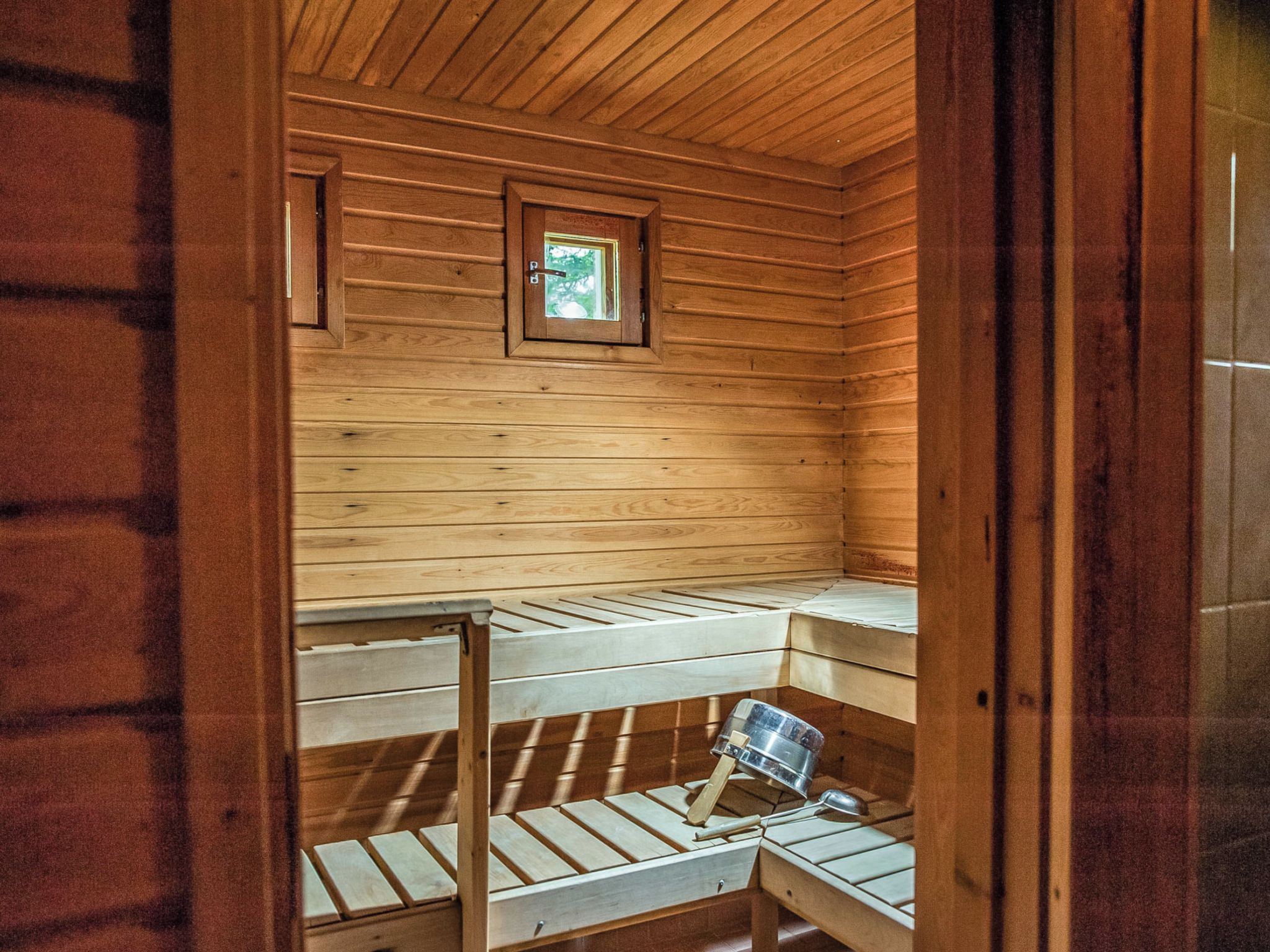 Interior de una cabaña de madera con literas, un ventanal pequeño y un cuadro en la pared.