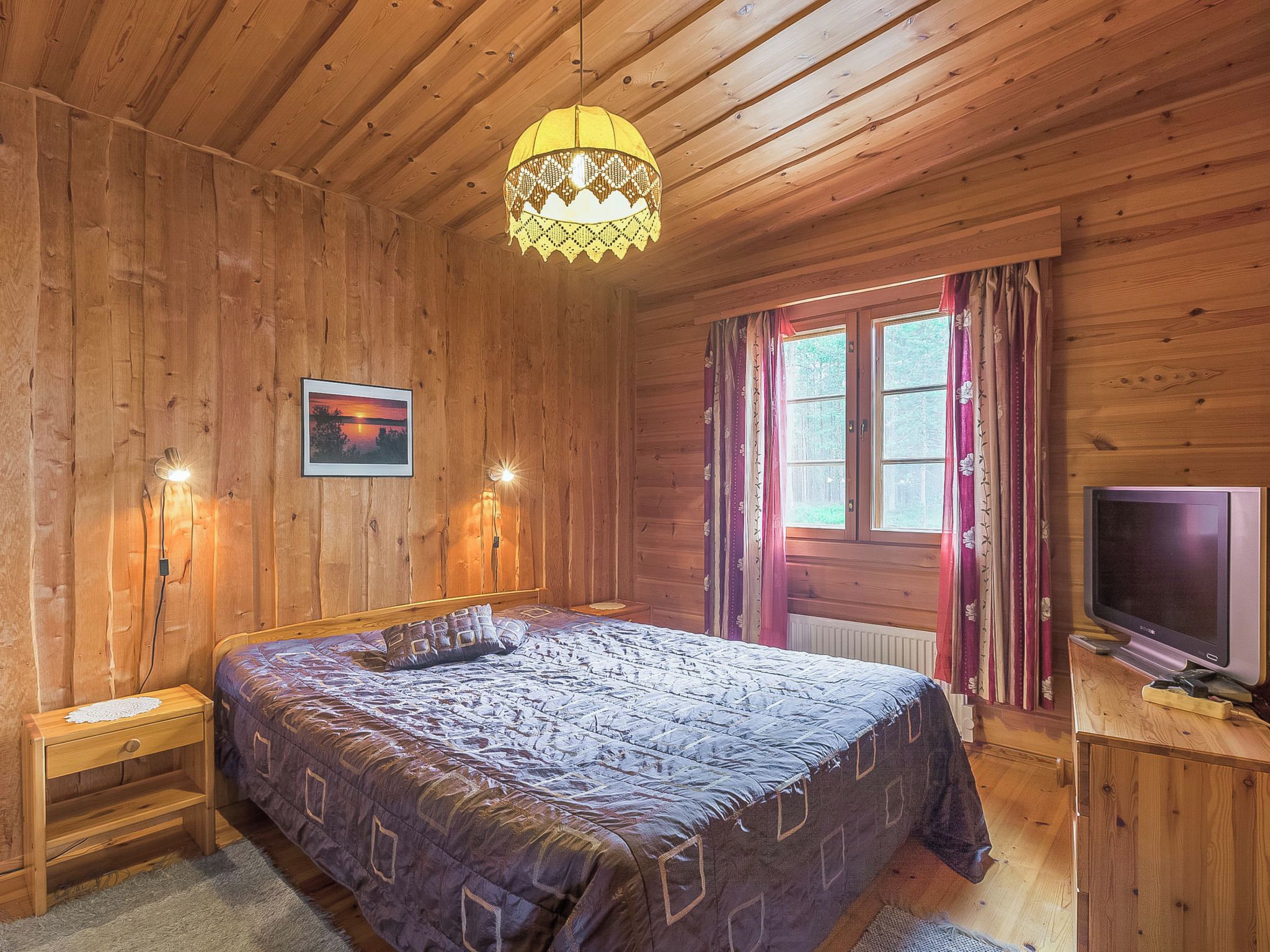 Una habitación de madera con una cama, un televisor y un ventanal con cortinas.