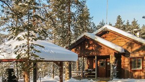 Una cabaña de madera con un porche cubierto y un techo cubierto de nieve, rodeada de árboles.
