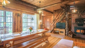 Interior rústico de una cabaña con pisos de madera, una larga mesa de comedor, bancos, una chimenea y un televisor.