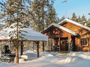 Une cabane en bois avec un porche, entourée d’arbres couverts de neige.
