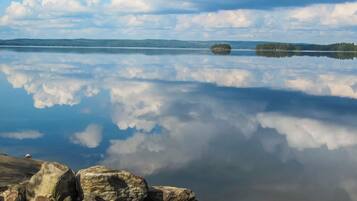 Un lago tranquilo con reflejos nítidos del cielo y las nubes, rodeado de rocas y árboles distantes.
