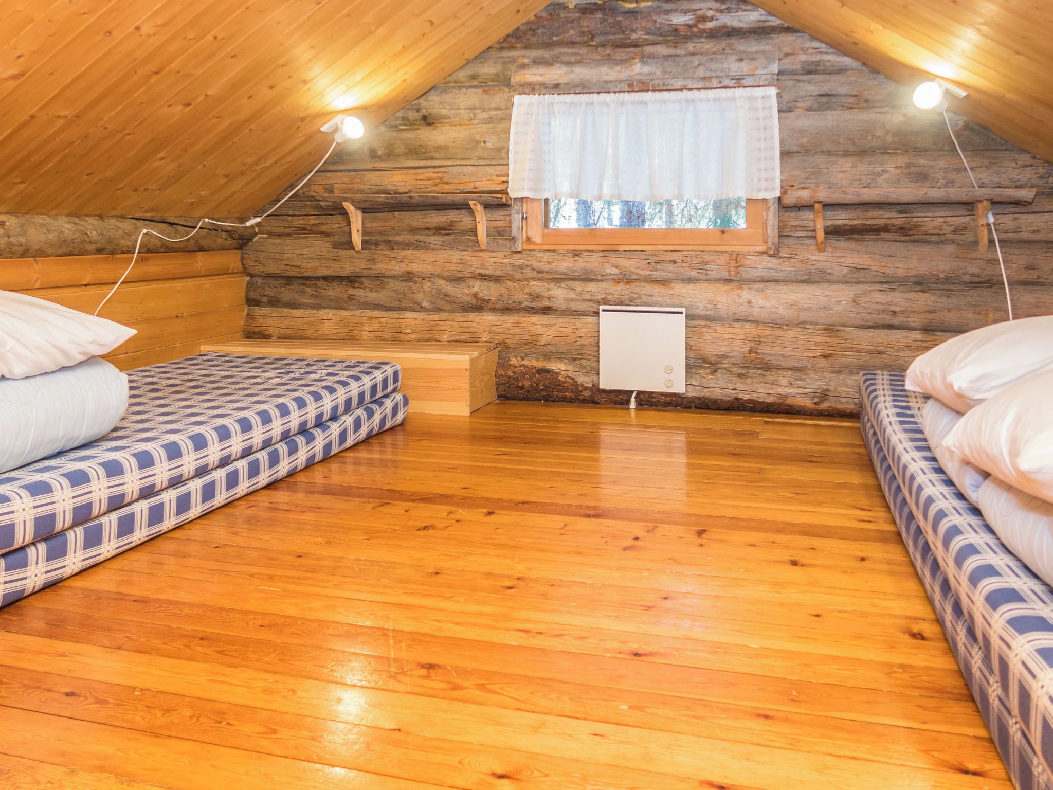 A cozy attic bedroom with wooden walls, a window with curtains, and two beds with patterned bedding.