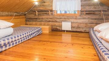 A cozy attic bedroom with wooden walls, a window with curtains, and two beds with patterned bedding.