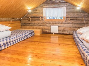 Un dormitorio acogedor en el ático con paredes de madera, una ventana con cortinas y dos camas con ropa de cama estampada.