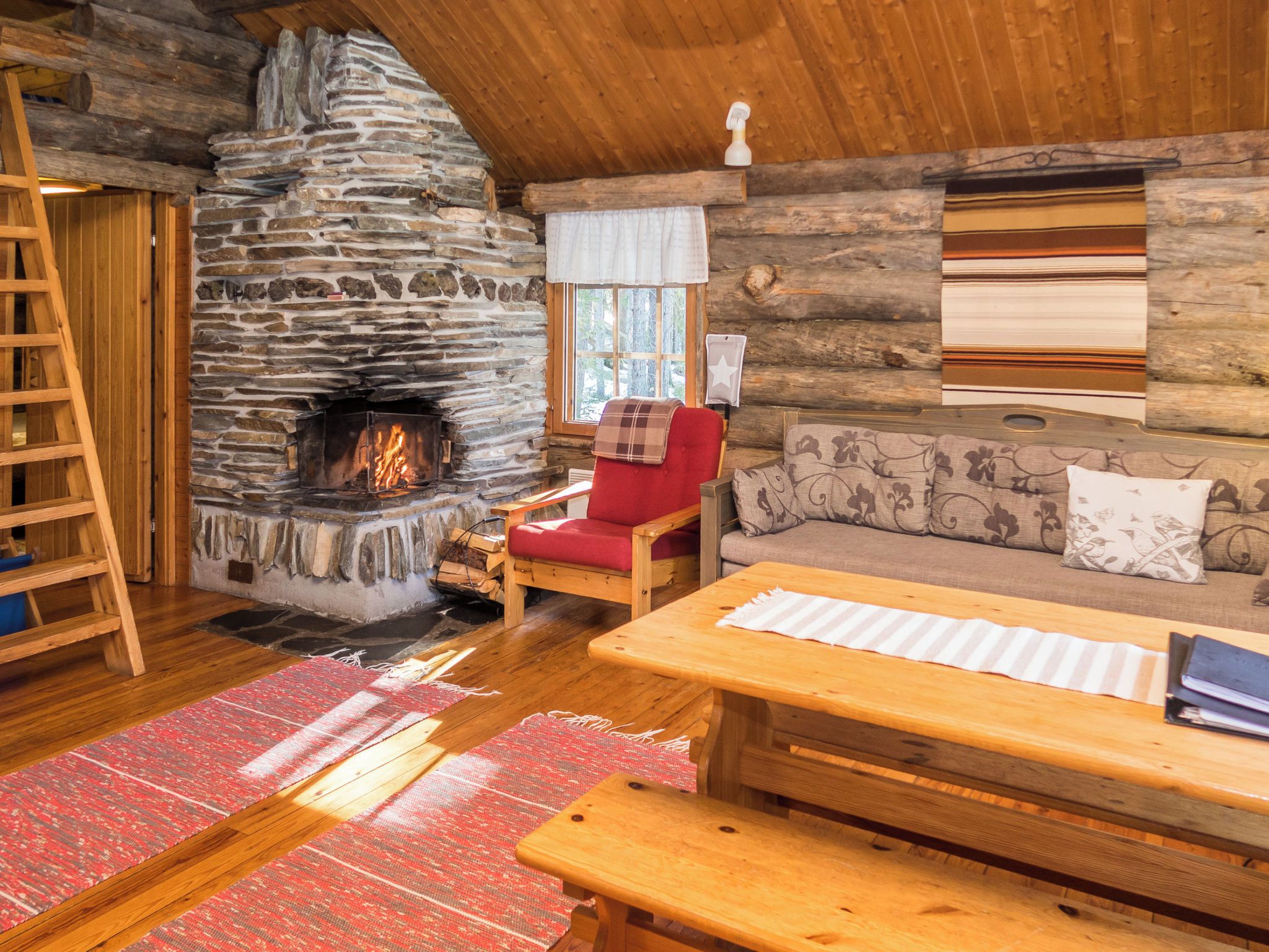A cozy cabin interior with a stone fireplace, wooden furniture, and a log wall.