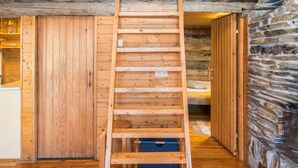 Una escala de fusta a una cabana de troncs amb una paret de pedra i terres de fusta.