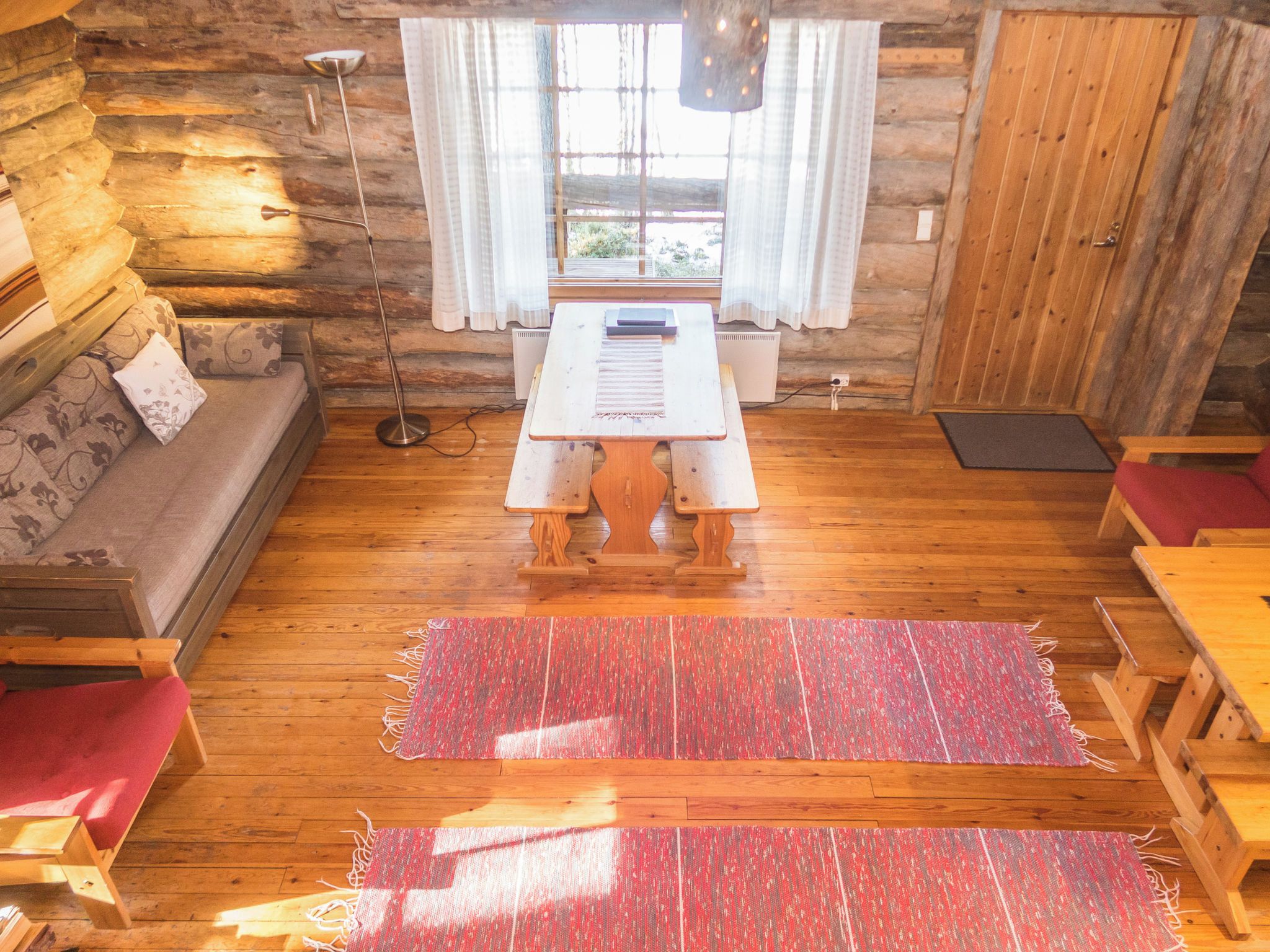 A cozy cabin interior with a wooden floor, a sofa, a table, and a window with curtains.