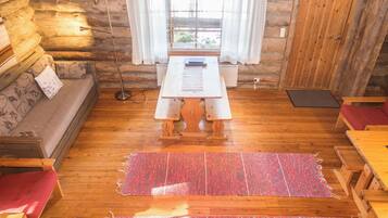 A cozy cabin interior with a wooden floor, a sofa, a table, and a window with curtains.
