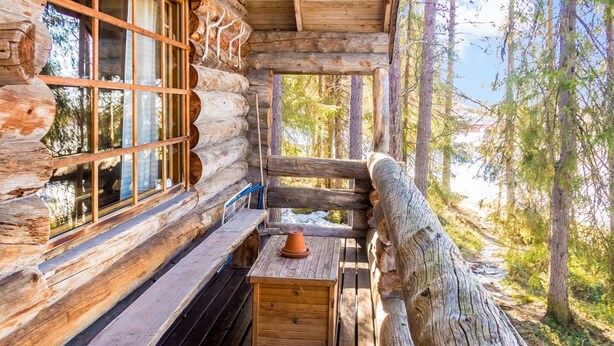 Una cabana de fusta amb una banca i taula de fusta, finestres grans i vista a la forest circumdant.