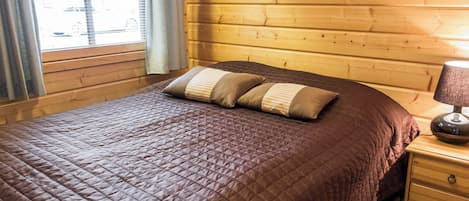 A wooden-paneled room with a bed, a nightstand, a lamp, and a window with curtains.
