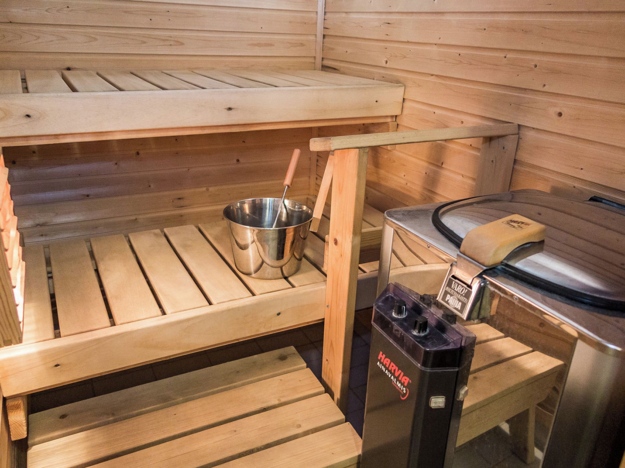 Een sauna met houten banken, een metalen wasbak en een sauna-oven.