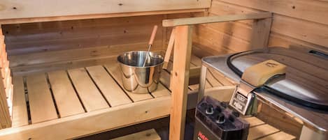 Un cuarto de sauna con bancos de madera, un recipiente metálico y un calentador de sauna.