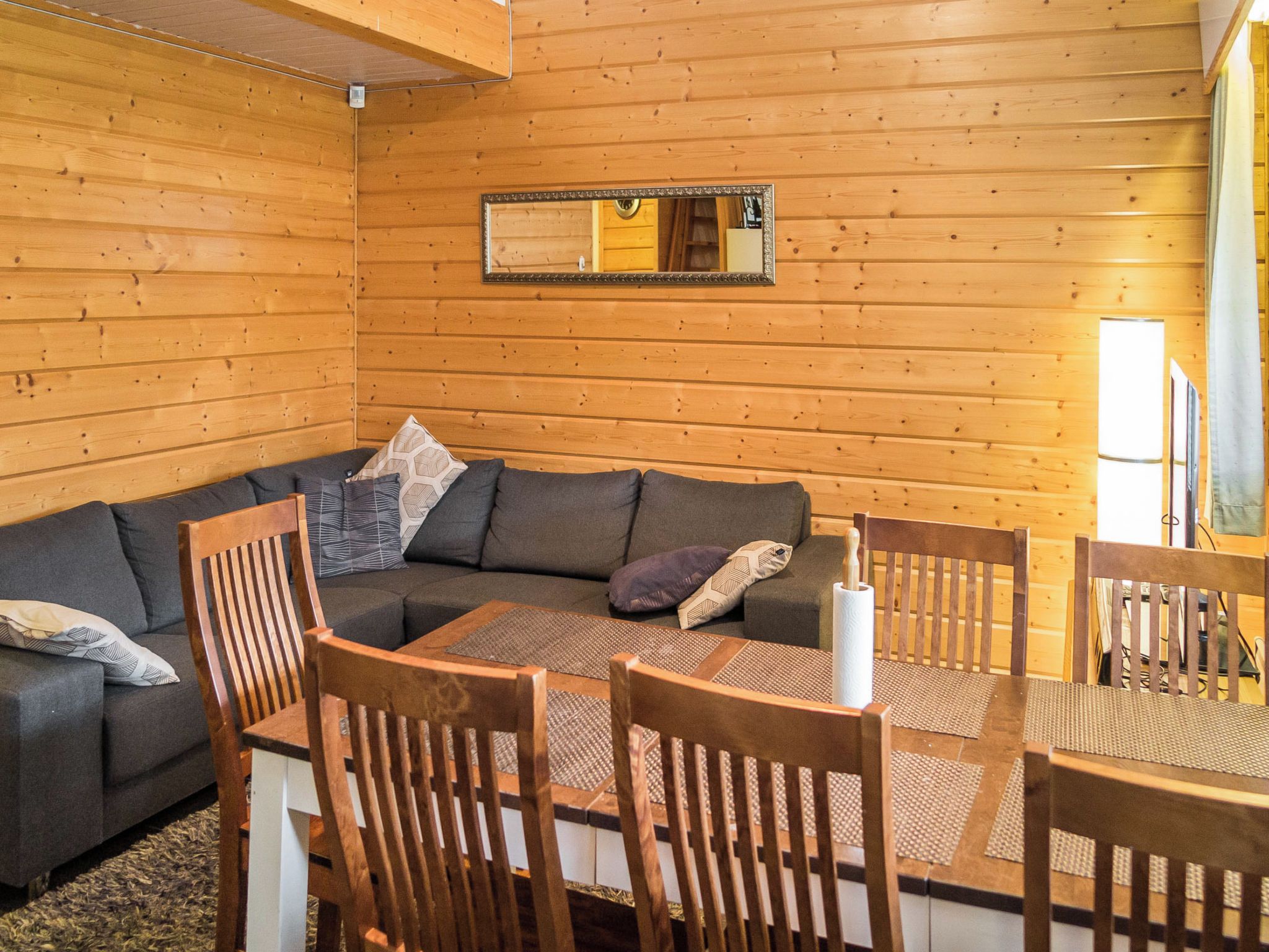 A cozy cabin interior with a wooden interior, a sofa, a dining table with chairs, and a mirror on the wall.