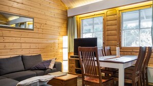 En mysig stuga med träpanel på väggarna, en soffa, ett matbord med stolar, en tv och ett fönster med persienner.