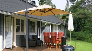 En uteplats med utemöbler, en grill och ett takförsett område med stolar och ett parasoll.