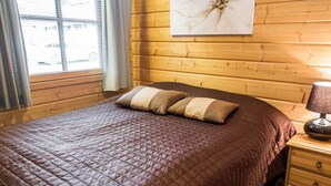 Ett rum med träpanel på väggarna, en säng, ett nattduksbord, en lampa och ett fönster med gardiner.