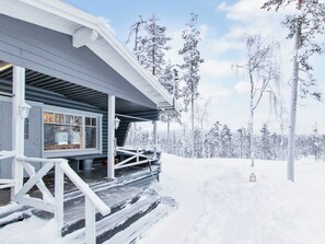 Une cabane dotée d’un porche abrité et offrant une vue sur une forêt enneigée.