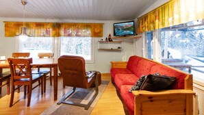 Een gezellige woonkamer met een houten plafond, een rode bank, een houten eettafel met stoelen en een televisie op een plank.